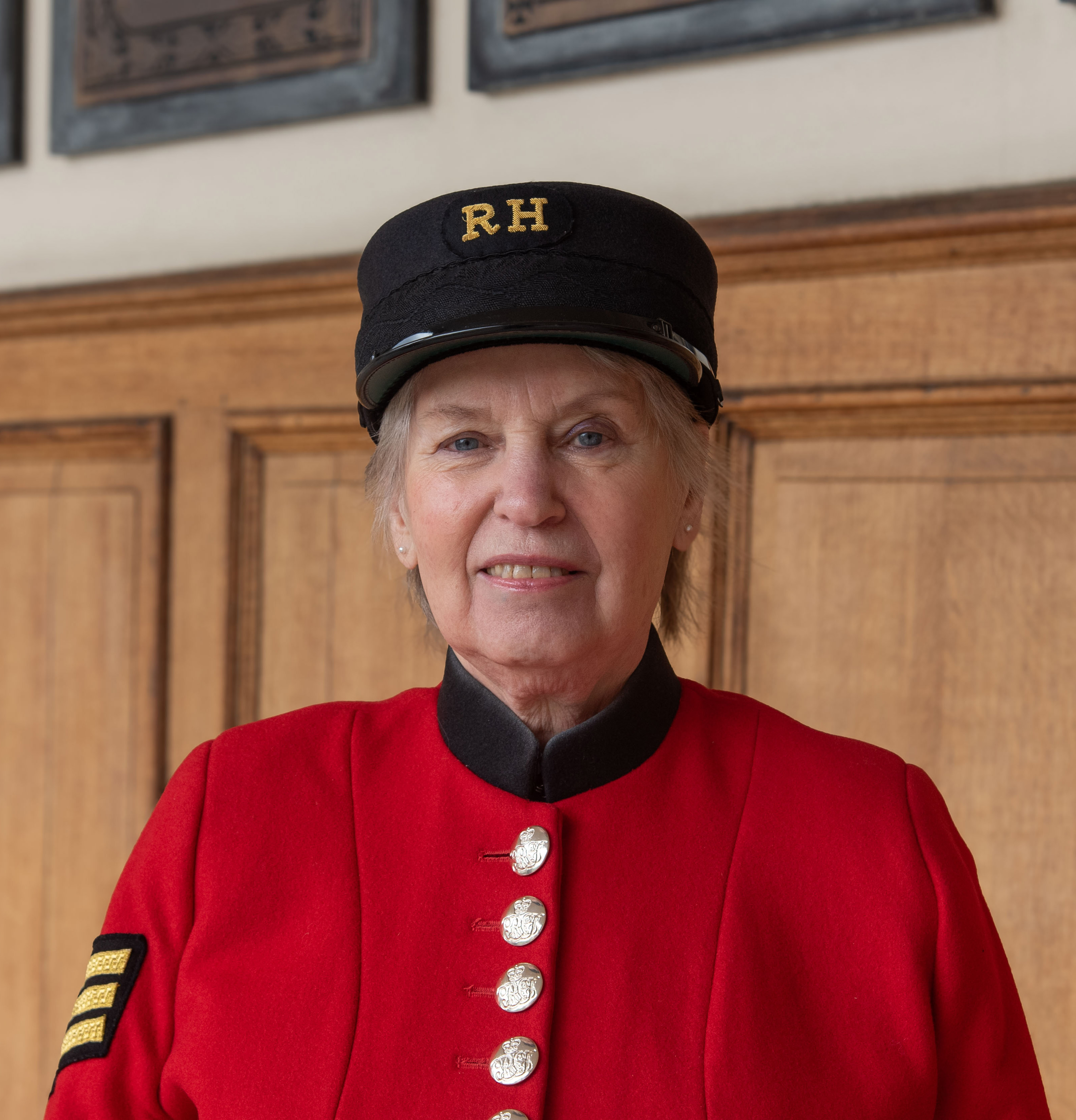 Female Chelsea Pensioner, Barbara Whilds, in Scarlet uniform and shako smiles at the camera