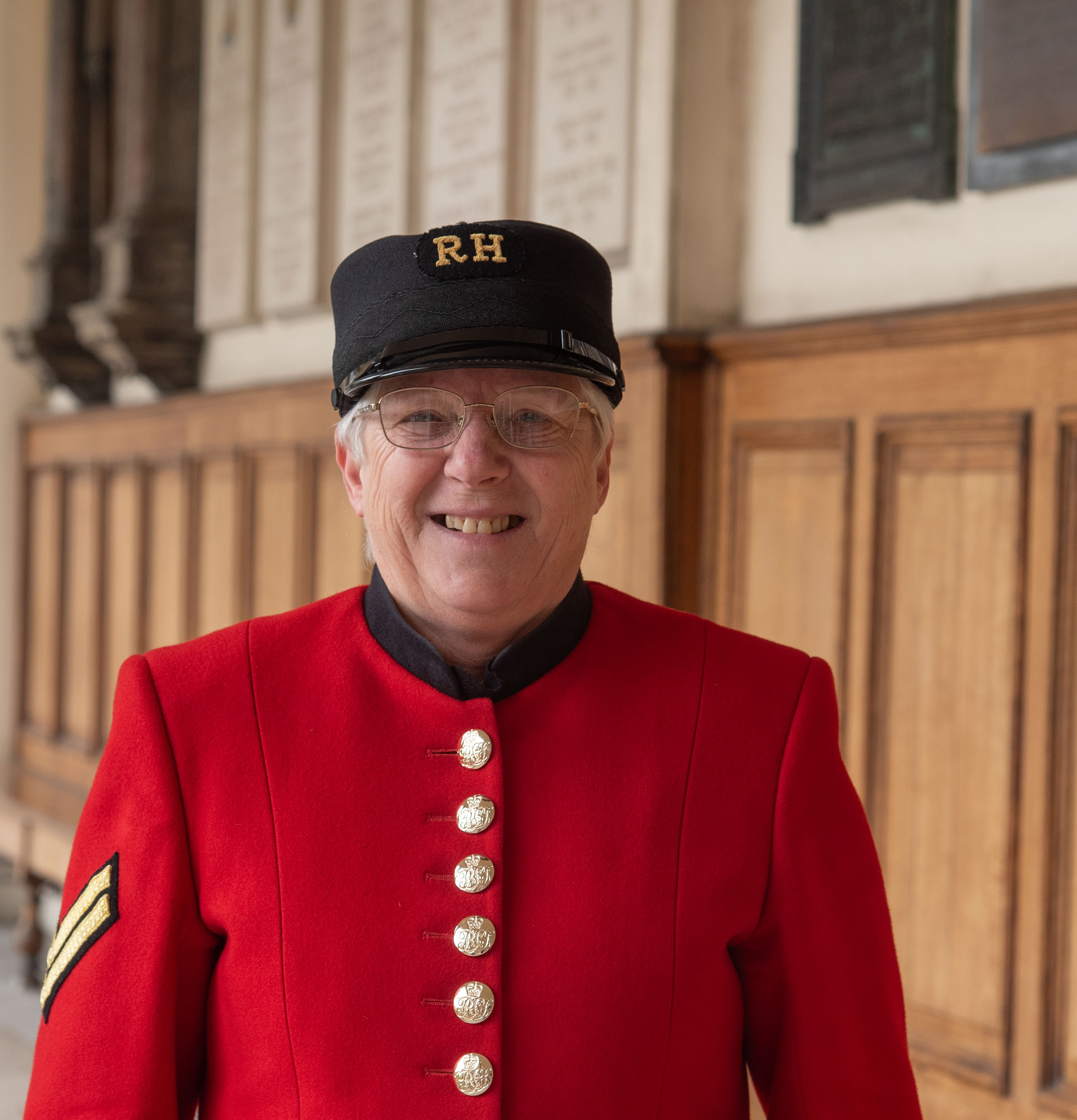 Female Chelsea Pensioner, Carol Knight, in Scarlet uniform and shako smiles at the camera