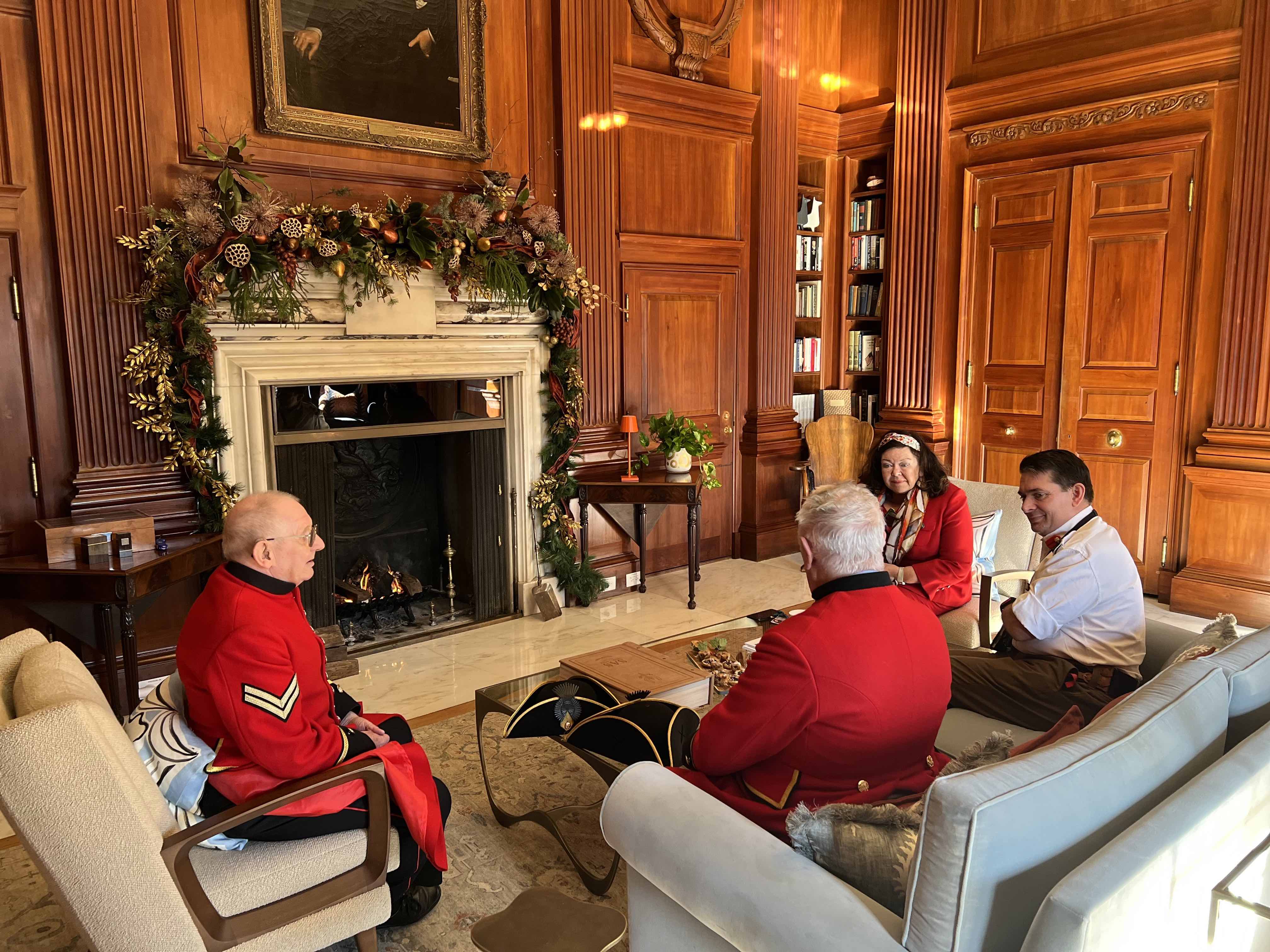 Chelsea Pensioners in Scarlet Uniforms sitting with the Lady Ambassador round a table