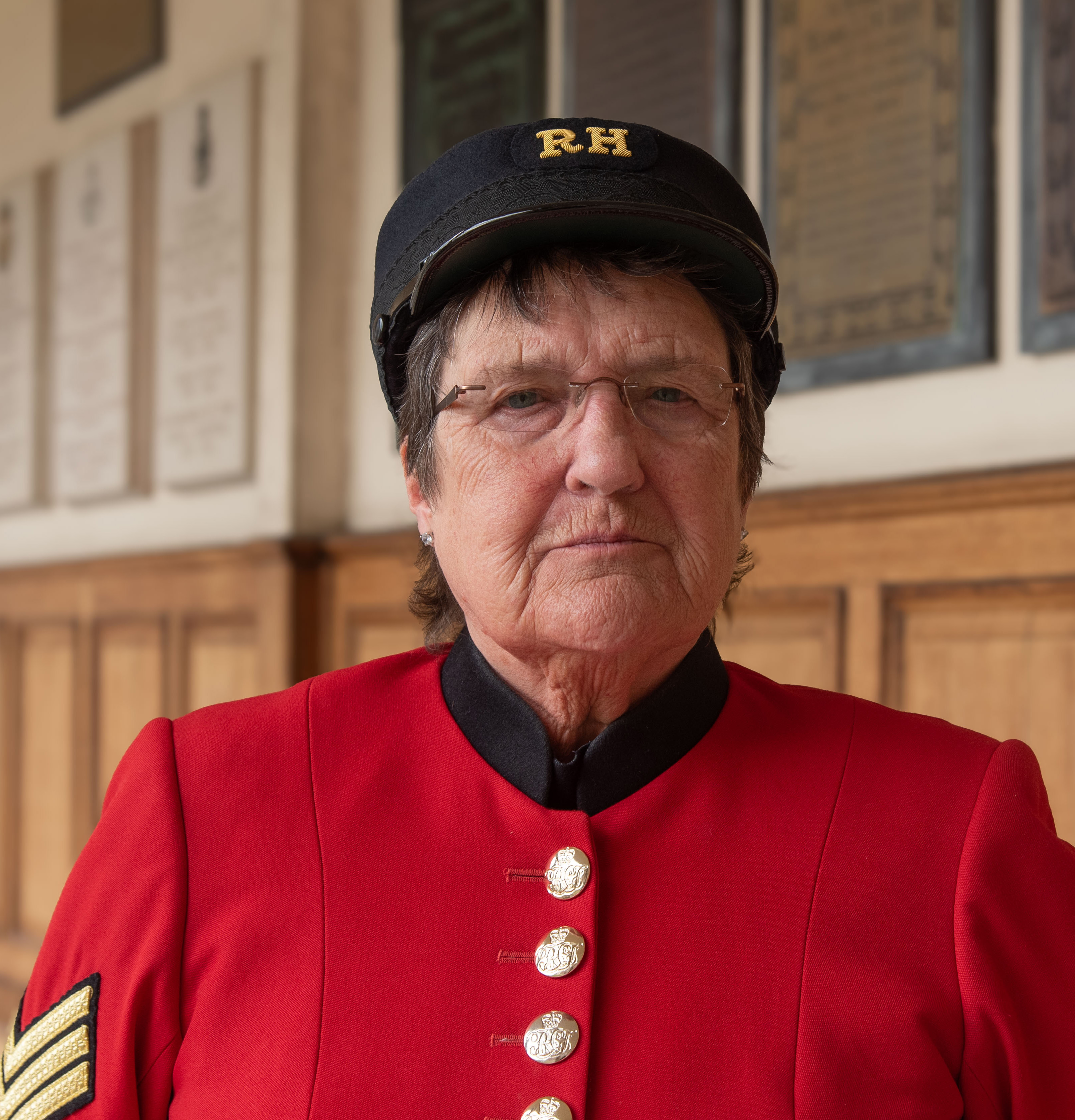 Close up of Chelsea Pensioner, Monica Parrott, looking at the camera in scarlet uniform and shako