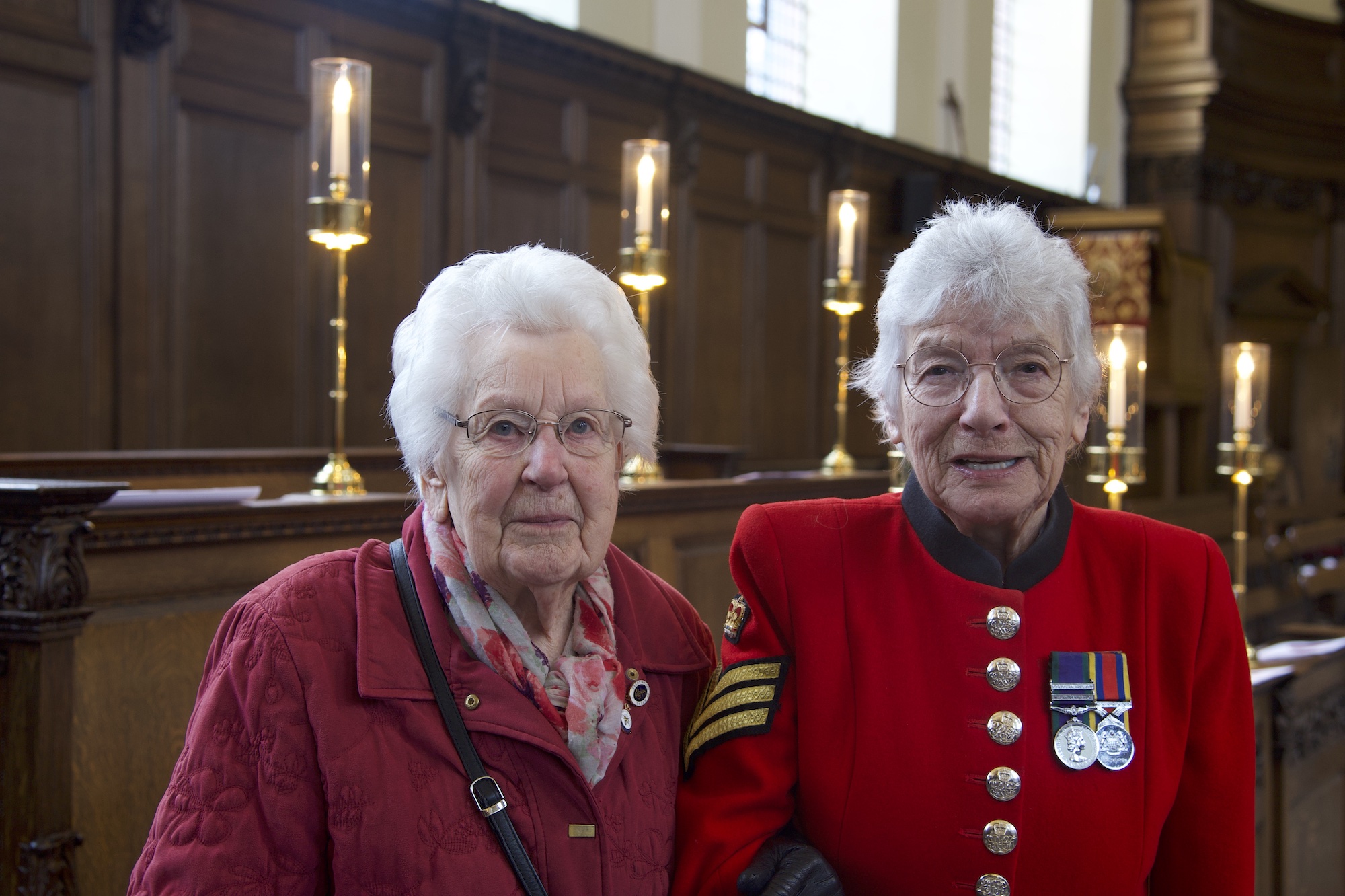 Two ladies standing together in a chapel, one in a Chelsea Pensioner scarlet uniform