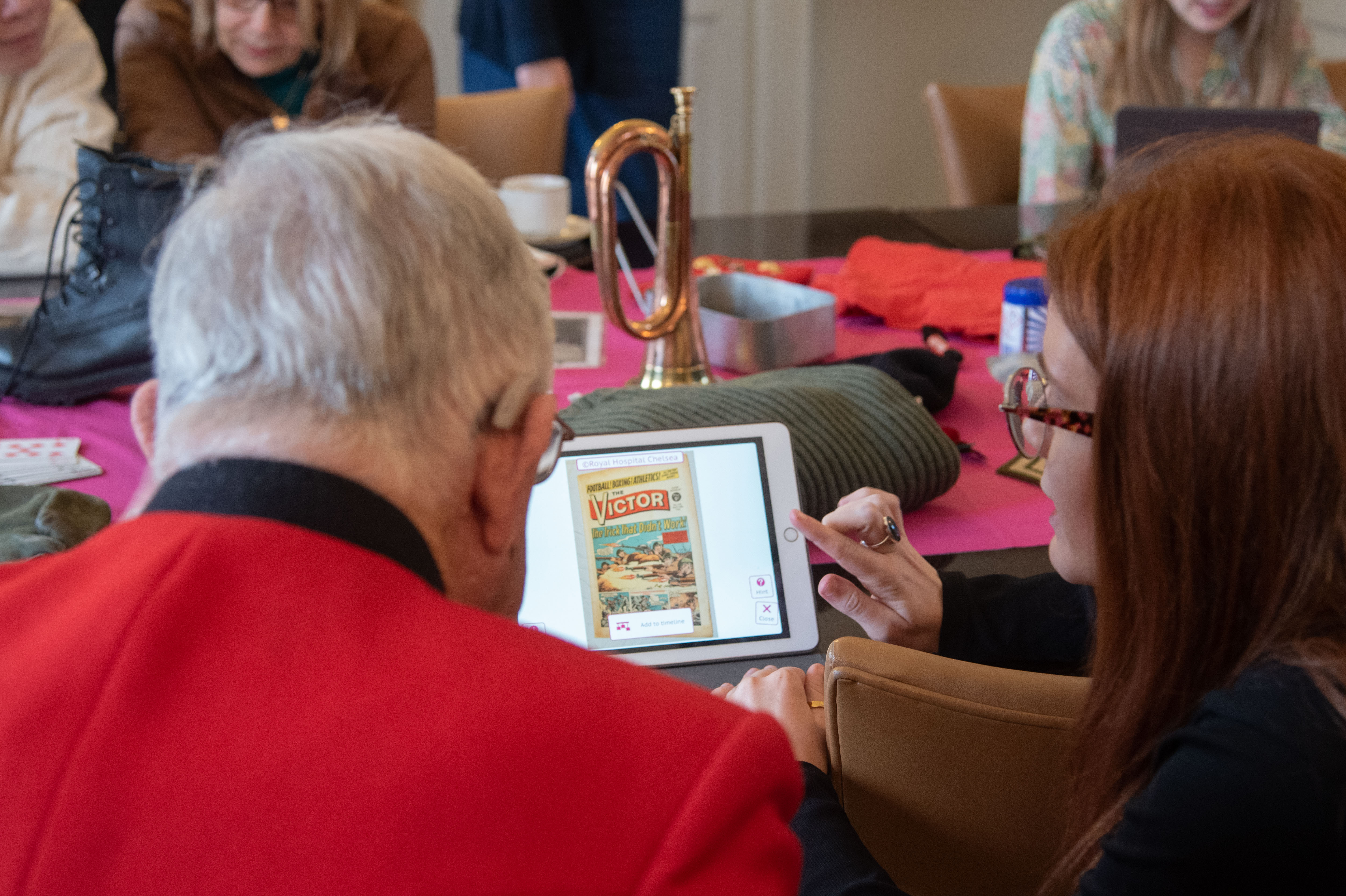 Chelsea Pensioner in scarlets and woman looking at an iPad