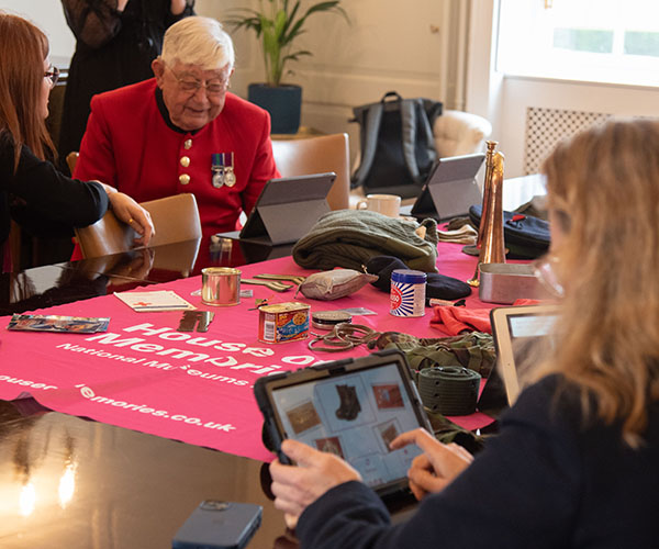 People sat round table looking at iPads. Pink House of Memories cloth in the middle with objects from the app on. 