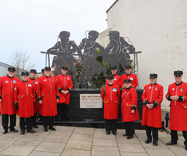 Group of Chelsea Pensioners stood in front of metal soldier sculpture