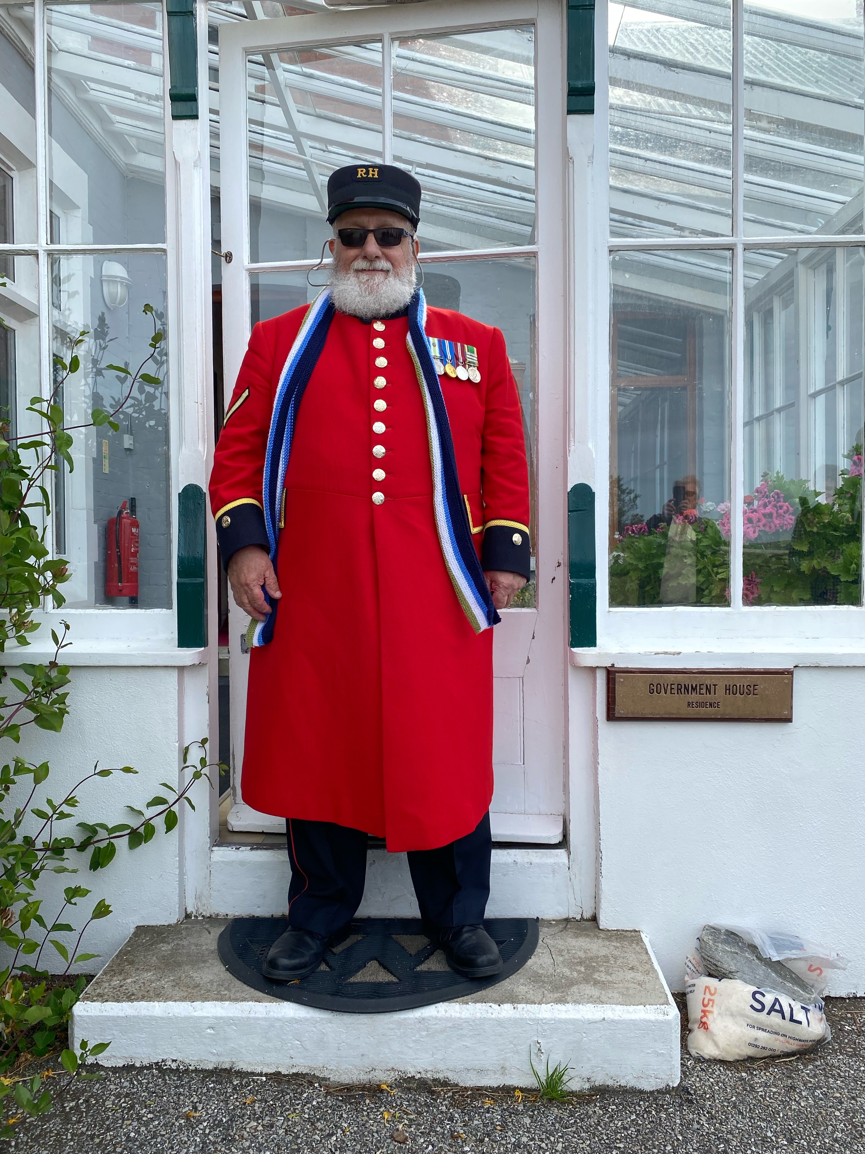 Chelsea Pensioner stood in front of glass door in scarlet uniform