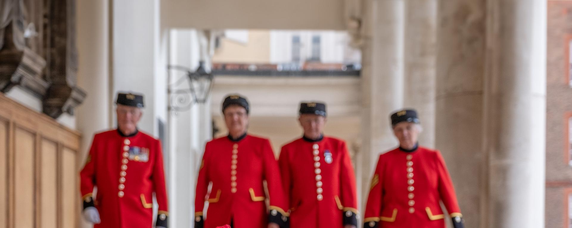 Scarlet coloured roses in the foreground as Chelsea Pensioners awash in Scarlet coats approach from the distance