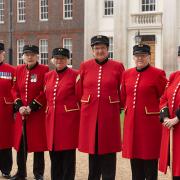 Female Chelsea Pensioners stood in front of Royal Hospital long ward in scarlet uniform and shako